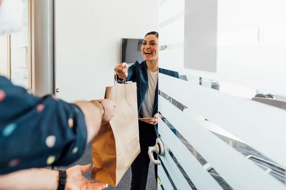 Happy delivery driver hands over a package, representing the strategic balance between first-party and third-party food delivery methods.