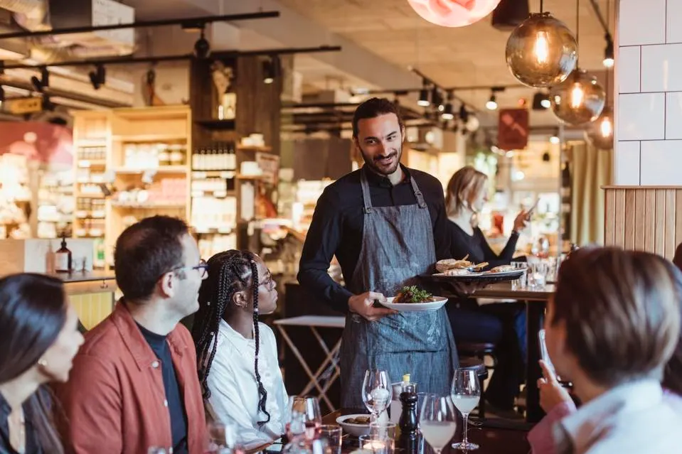 Waiter serving food to customers during party in restaurant